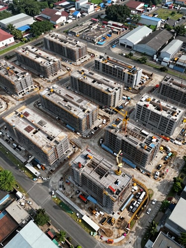 Drone overhead perspective of a large industrial-commercial development site in Surabaya, multiple building blocks under structured construction, site boundary clearly visible, natural daylight from above, no rendering or CGI, real construction activity visible