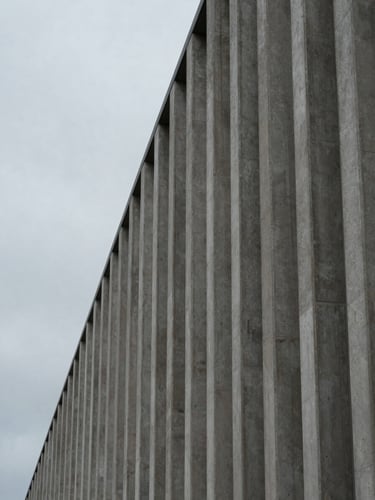 Panoramic architectural detail in the Pacific Northwest — a concrete facade under flat overcast sky, left third open grey atmosphere, strong vertical lines of the structure occupying the right two-thirds, no direct sun, muted tonal range