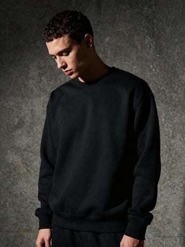 Stoic model in a heavyweight black structured sweatshirt looking down, dramatic side-lighting casting deep shadows, raw concrete background, 35mm film grain