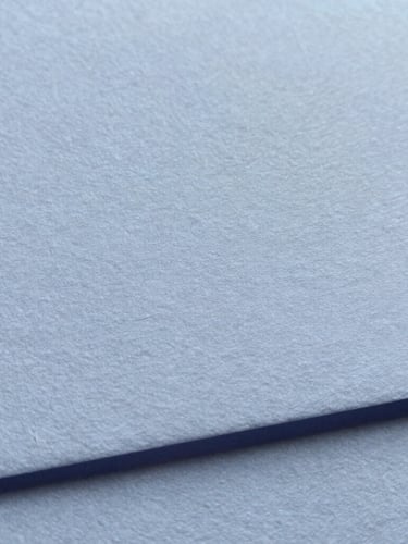 Close-up of premium textured cotton paper collateral with blind debossing, soft overcast daylight, muted blue and charcoal tones, macro shot