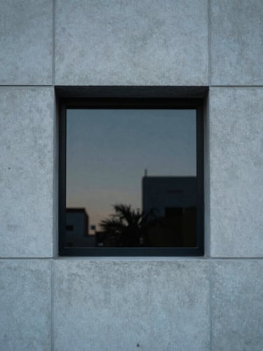 Tight architectural crop of a minimalist concrete facade in Miami, soft diffused late-afternoon window light, muted blue and charcoal tones, 35mm