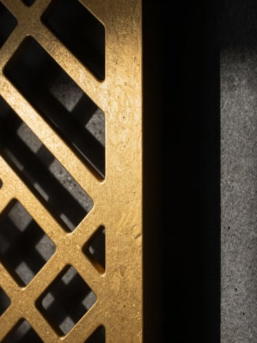 Macro close-up shot of a laser-cut gold anodized metal screen, sharp geometric shadows cast on a dark concrete wall, high-contrast dramatic lighting, architectural details