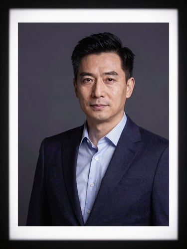 Executive headshot framed tightly from chest up against a deep charcoal studio backdrop, single hard key light from camera-left casting clean shadow definition, professional business attire, color grade with cool purple undertones