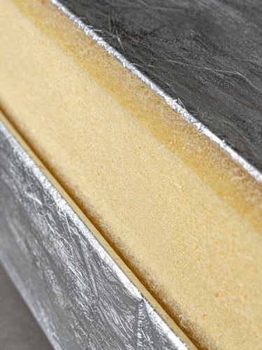Extreme close-up of a pre-insulated duct panel, showing the high-density yellow polyisocyanurate foam core sandwiched between textured double-sided silver aluminum cladding, sharp industrial lighting highlighting the cellular structure.