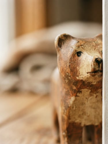A tight macro shot of a hand-painted wooden toy kissing the right canvas edge, natural window light showing rich wood grain and lacquer imperfections, warm earthy tones.