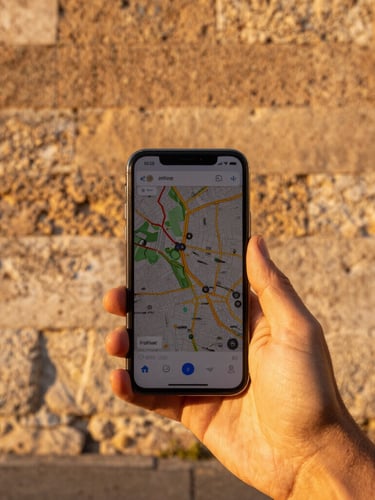First-person perspective of a hand holding a smartphone displaying offline maps against a historic Roman stone wall, golden daylight.