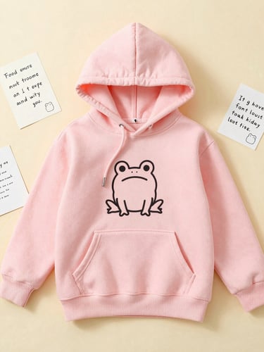 A top-down flat-lay of a pastel pink hoodie with a small black ink doodle of an anxious frog, surrounded by cute handwritten cards, soft diffused daylight.