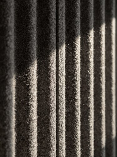 Close-up of dense charcoal wool acoustic tile showing rich textile grain and clean edge joinery, dramatic side lighting