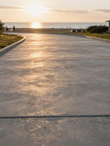 Low-angle shot of a clean, finished concrete driveway with sharp borders, golden hour light reflecting on the stone, Lubmin coast in the background.