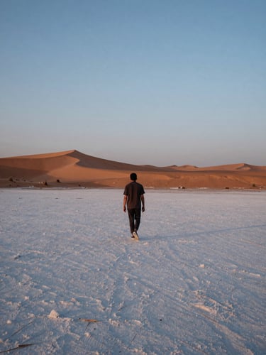 Cinematic 35mm photograph of a solitary traveler walking towards the horizon on the white salt desert of Kutch at twilight, soft blue hour light, minimal composition, warm sand tones.
