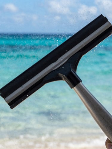 Extreme close-up of a squeegee wiping clean a salt-encrusted glass pane, revealing a sharp reflection of the turquoise Caribbean ocean, bright coastal light.
