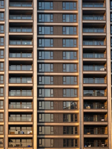 Symmetrical architectural shot of a modern luxury residential tower facade at golden hour, deep navy shadows and warm golden light reflecting off glass panels.