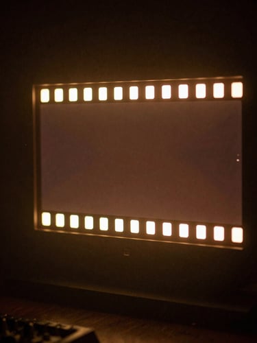 A low-key cinematic director's monitor glowing in a dark studio haze, displaying a high-contrast anamorphic film frame, warm amber backlighting, 35mm grain.