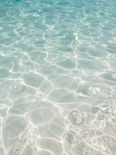 Extreme close-up of crystal-clear Maldivian water rippling over white sand under soft morning light, ocean-tinted tones.