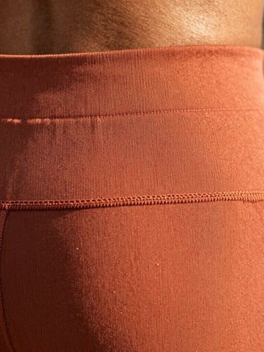 Macro detail of high-quality flatlock stitching on a terracotta activewear waistband, warm natural sunlight, shallow depth of field