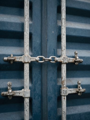 Close-up macro detail of heavy steel shipping container locks and chains, cool overcast daylight, desaturated steel and navy tones, sharp focus, 35mm.