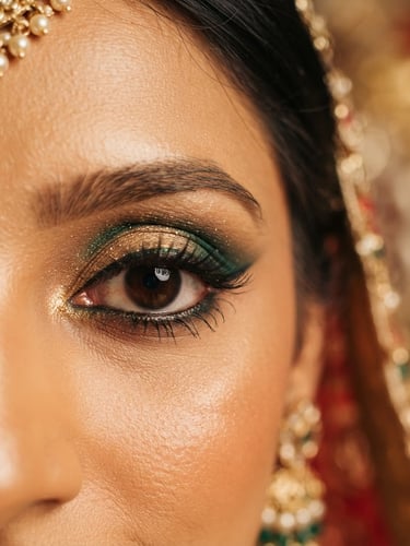 Close-up of an Indian bride's eye, intricate gold and emerald green eyeshadow, fine eyeliner, and perfectly shaped brows, soft golden studio light, shallow depth of field, 85mm portrait lens, warm editorial photography, rich saturated jewel tones