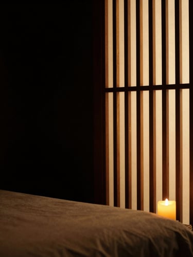 Chiaroscuro shot of a minimalist luxury massage room, warm light filtering through a wooden screen, absolute peace
