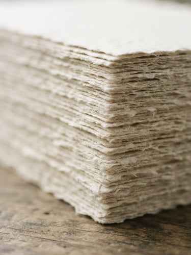 Macro shot of heavy-weight paper sheets stacked, soft north-facing daylight casting gentle shadows on the textured edges, 35mm photography