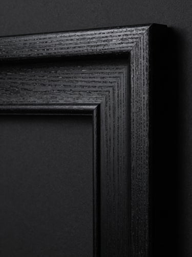 Extreme close-up of a black wooden frame corner resting against a dark studio wall, hard directional light highlighting the wood grain and deep chiaroscuro shadows.