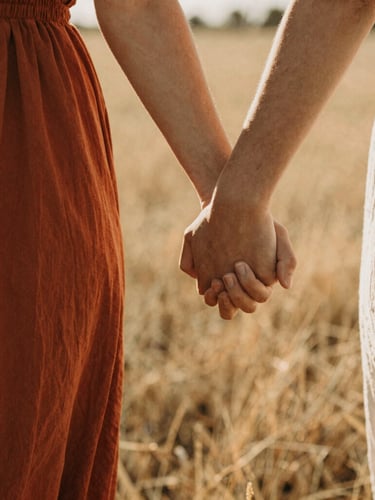 Intimate close-up of a couple holding hands, walking through a sunlit field, warm golden light, shallow depth of field, 35mm film grain, cinematic