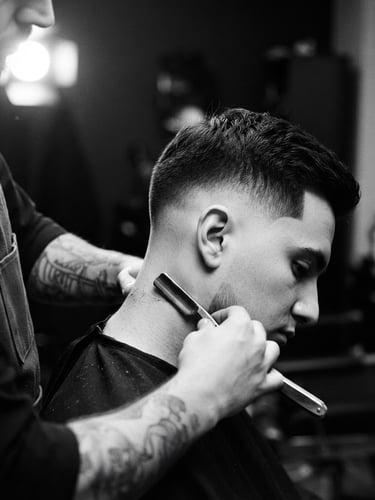high-contrast black and white photography, dramatic side-lit studio lighting, luxury minimalist mood, sharp focus, 35mm film. A close-up of straight-razor precision grooming on a client, sharp hair fade, elegant monochrome tones.