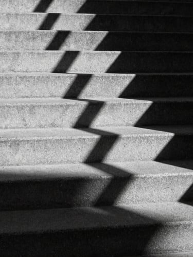Stark black and white architectural shadows cast on concrete steps, high-contrast chiaroscuro, sharp focus, geometric lines, 35mm film
