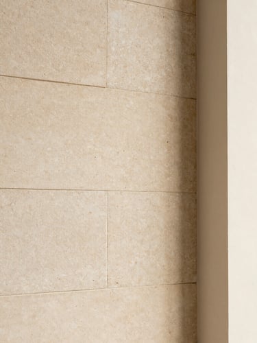 Detailed close-up of premium warm limestone block wall meeting smooth plaster, soft natural side lighting, minimalist architectural detail.