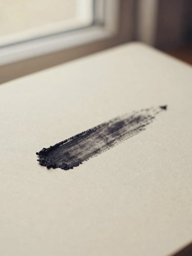Close-up of a charcoal smudge on a warm cream paper journal, soft morning window light, shallow depth of field, muted earth tones