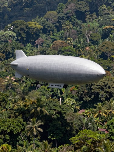 Extreme wide-angle portrait shot of the FLYING WHALES airship hovering over a dense tropical forest canopy in Indonesia, bright natural daylight