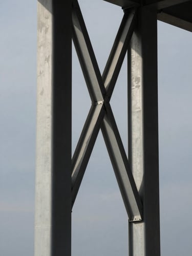 Architectural detail of structural steel columns intersecting under a cool overcast sky, high contrast, sharp shadows, vertical composition.