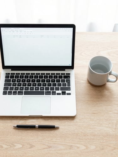Overhead flat-lay of a clean Nordic workspace, a laptop displaying a simple spreadsheet, a black pen, and a ceramic mug on a light oak desk, bright natural overcast daylight