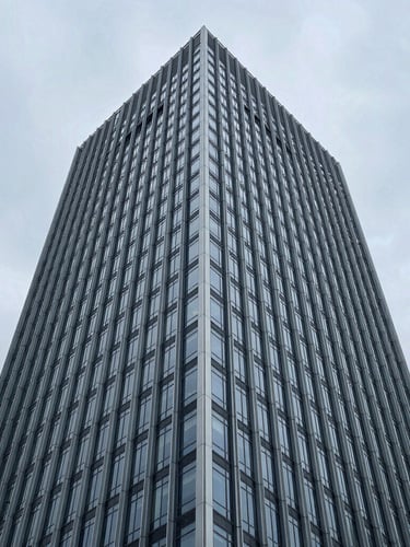 High-angle architectural detail of a modern steel and glass skyscraper facade against a cool overcast sky, clean geometric lines.