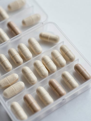 Close-up overhead view of a pill organizer with sorted tablets on a clinical white surface, studio daylight rendering each capsule's detail sharply, no hands visible