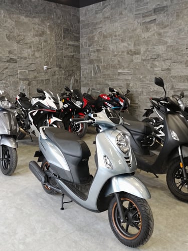 Wide shot of a clean motorcycle showroom interior, organized sections of automatic scooters and sportbikes, modern garage design with slate-grey walls, bright natural light