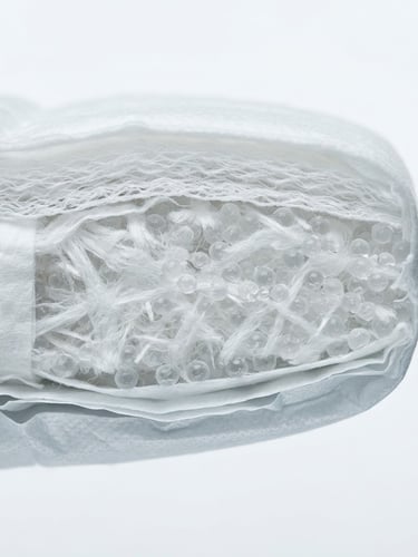 Macro close-up of a multi-layer baby diaper cross-section, showing engineered absorption core, clinical studio lighting, sterile white background, cool tones.