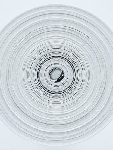 Macro close-up of tightly wound, multi-layered paper roll, showing fine, consistent texture under bright clinical studio light, cool white tones, centered architectural framing.
