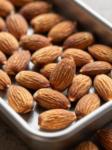 Macro close-up of graded California almonds in a steel sorting tray under bright morning light.