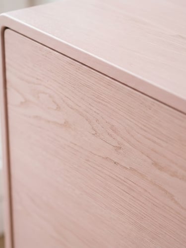 Close-up detail of smooth pastel pink wood grain on a furniture piece, soft morning daylight, clean composition.