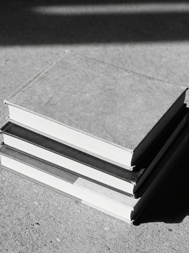 Stark monochrome photograph of multiple books stacked on a raw concrete surface, harsh side shadows, grainy film texture.