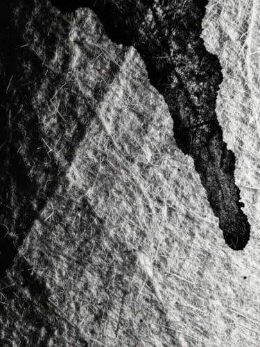 Extreme close-up of textured heavy cotton paper with dark black ink bleeding into the fibers, high-contrast side lighting, deep shadows, grainy 35mm film texture