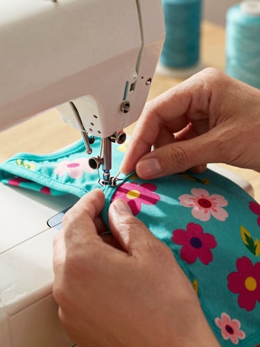 Close-up of hands carefully sewing a colorful floral dog shirt on a vintage sewing machine, bright warm natural daylight, teal threads visible, 35mm