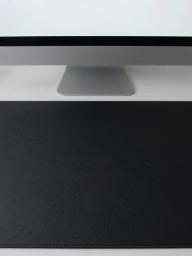 Top-down view of a clean minimalist desk setup, single sleek monitor displaying plain text, matte black desk mat, soft natural side light