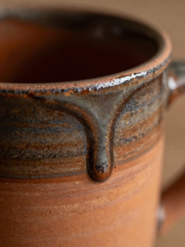 Extreme macro shot of a ceramic glaze drip frozen on the rim of a terracotta mug, showing rich texture and deep kiln-fired colors, shallow depth of field