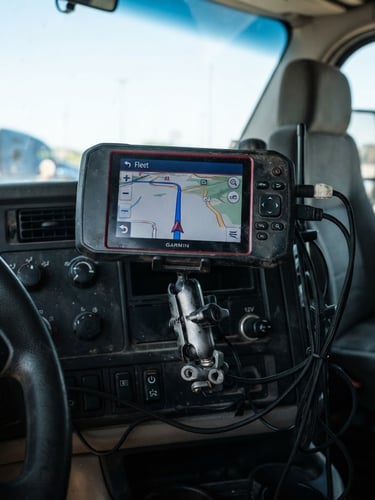 Close-up of a heavy commercial tractocamión cabin parked under sharp daylight, focusing on the rugged GPS hardware installed on the dashboard, 35mm lens, high-contrast technical details.