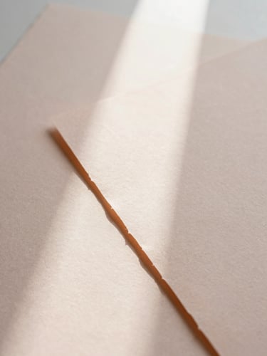 Close-up of textured handmade paper sheets with deckled edges, soft shadows from morning window light casting across a pale apricot surface, elegant minimalist composition, 35mm.