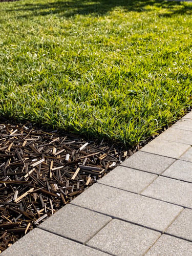Bright outdoor photography of a beautifully manicured lawn with a newly installed gray stone paver walkway, warm afternoon sunlight, vibrant green grass and rich dark mulch, sharp focus, 35mm
