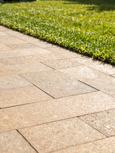 A stunning newly laid stone paver patio in warm afternoon sunlight, clean geometric lines, lush green lawn in the background, sharp focus, 35mm