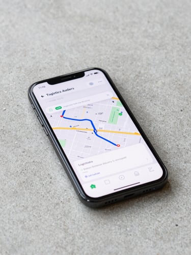Wide shot of an Android phone resting on a bare concrete surface, screen showing a logistics tracking app with a single active-route map and minimal chrome, bright neutral daylight from the left