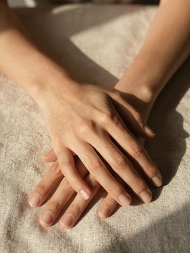 Detail of hands resting gently on a textured linen fabric, warm afternoon light creating soft shadows, intimate and calm atmosphere